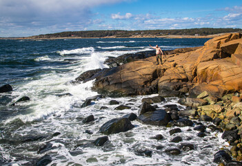 Fototapeta na wymiar A man on a rocky beach. Waves smashing against the rocks. 