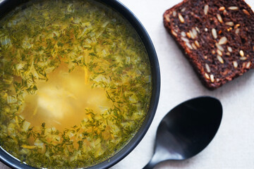 Chicken soup with greens and grain bread and black spoon on gray background
