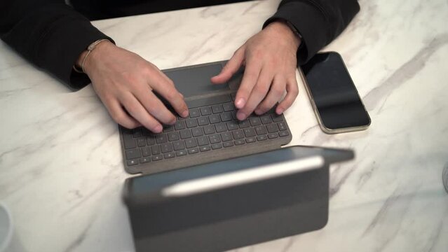 Toma en 4k de persona tecleando en un teclado de tablet en mesa de diseño