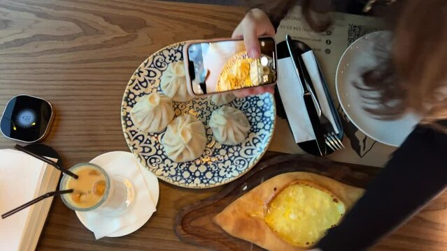 a girl's hand takes pictures of food in a Georgian restaurant, khachapuri Khinkali water with lemon and aislate take photos and videos for social networks on Internet blog. blogger Food