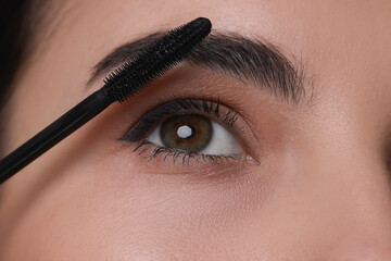Beautiful young woman applying mascara, closeup view