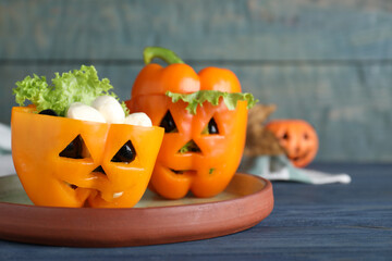 Bell peppers with black olives and lettuce as Halloween monsters on blue wooden table