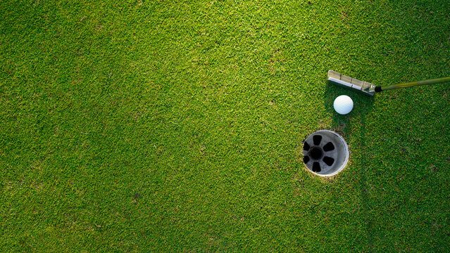 Top view of a golf ball with putter on green course at hole.