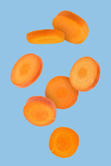 Fresh carrot slices falling on light blue background