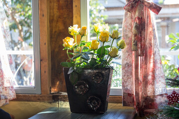 Pot of yellow roses placed next to a sunny window