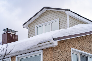 Corner of house with roof made of red metal tiles, chimney and gutter covered with thick layer of snow in winter. Metal Downpipe system, Guttering System, External downpipes and drainage pipes