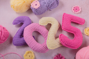 New Years background 2025. Multicolored crochet numbers, skein of wool yarn and knitting needles on gray background. New Years start creative handcrafted idea for DIY crafters