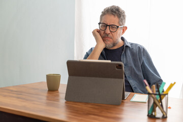 Man focused on digital learning from home, engaging with content on a tablet for personal development.