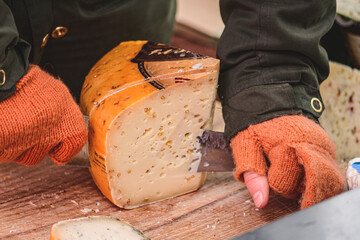 Hands of woman cutting with a knife a slice of homemade bio natural Latvian cheese in a street food market 