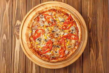 delicious pizza with chicken, mushrooms, cheese, tomatoes and corn on a wooden background