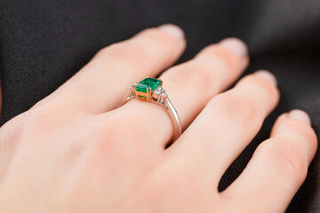 Beautiful female hand with gold ring with diamonds and emerald on gray background