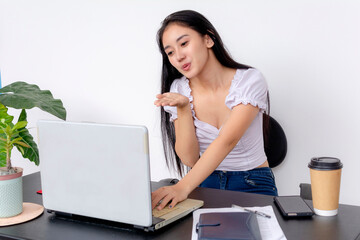 A focused young female college student works at her desk with a laptop, textbooks, and a coffee cup. Plain white background.