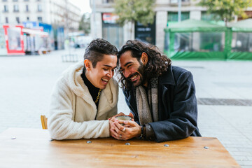 Happy gay couple enjoying having a date sitting outdoors at a coffee shop.