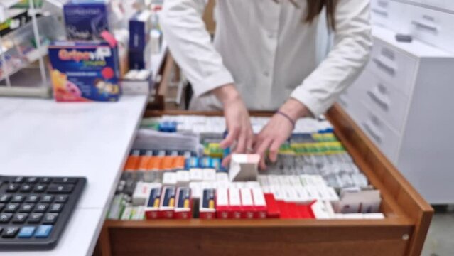 Defocused view inside of pharmacy with female pharmacist stores the medicine inside the drawers and shelves. Healthcare and cosmetics industry blurred background
