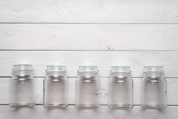 Empty glass jars on the white wooden desk table flat lay background with copy space.