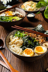 Traditional ramen with jerked pork or chicken.  With udon or ramen noodles. Served in classic bowls. Gyoza dumplings and mushrooms in the background.