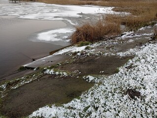 The shore of a frozen winter lake with concrete shores. Winter landscape of a reservoir with the surface part covered with ice.