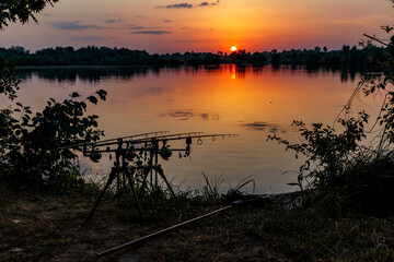 Obraz premium Fishing adventures, carp fishing. Angler, at sunset, is fishing with carpfishing technique. Camping on the shore of the lake.Carp Fishing Sunset