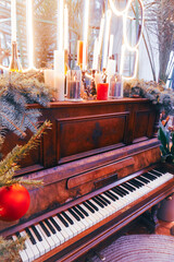 An old piano made of mahogany stands in front of a Christmas tree, decorated with various holiday...