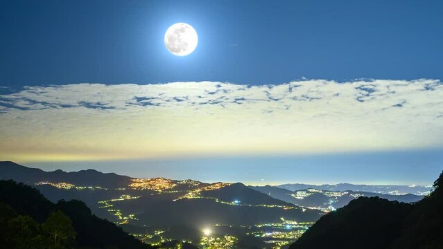 Stunning views of the full moon illuminate the tranquil landscape of the mountains, highlighting the city lights amid natural beauty. New Taipei.