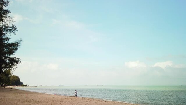 Dynamic timelapse captured during a partly cloudy day at Pantai Puteri Beach in Melaka, Malaysia, with fast-moving people. The scene includes green trees and a bustling road beyond the shoreline.