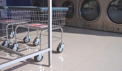 Two laundry basket trolleys on tile floor with row of vending washing machines and clothes dryer inside of modern laundromat shop