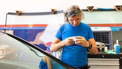 A man in a blue t-shirt wears safety glasses for work and a black watch on his left hand, using a...
