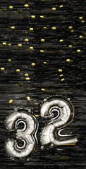Silver foil balloon number 32 on a background of black tinsel with gold confetti. Birthday card,...