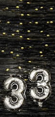 Silver foil balloon number 33 on a background of black tinsel with gold confetti. Birthday card,...
