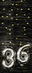 Silver foil balloon number 36 on a background of black tinsel with gold confetti. Birthday card,...