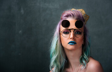 Woman With Blue and Green Hair Wearing Glasses. Portrait of a woman with blue and green hair, wearing glasses, in front of a neutral background. - obrazy, fototapety, plakaty