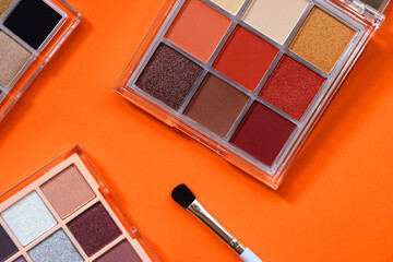 Colorful eyeshadow palettes and make up brush on orange background. Top view.