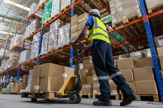 Man African American worker wear safety uniform push load cart product to shelf in warehouse store. Company employees arrange products. Warehouse industrial stock storage.
