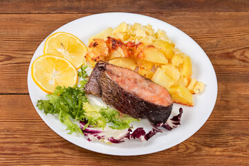 Trout piece baked with potato, served with greens and lemon
