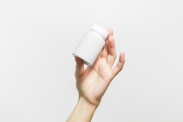 hand holding a white plastic jar with pills