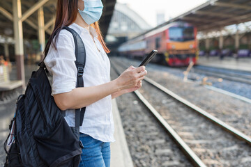 Woman traveler waiting on station waiting for a train while using a smartphone. Backpacker female plan route of stop railway. Railroad transport and booked. The concept of a woman traveling alone.