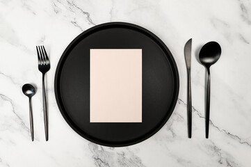 Top view of black cutlery and black plate on white marble background. Light pink blank, card flat lay. Copy space.