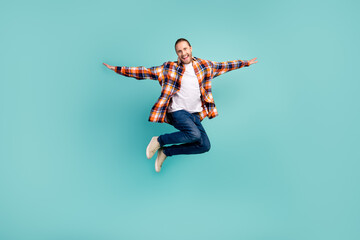 Full length photo of overjoyed man wear flannel shirt denim trousers flying hold hands like wings...