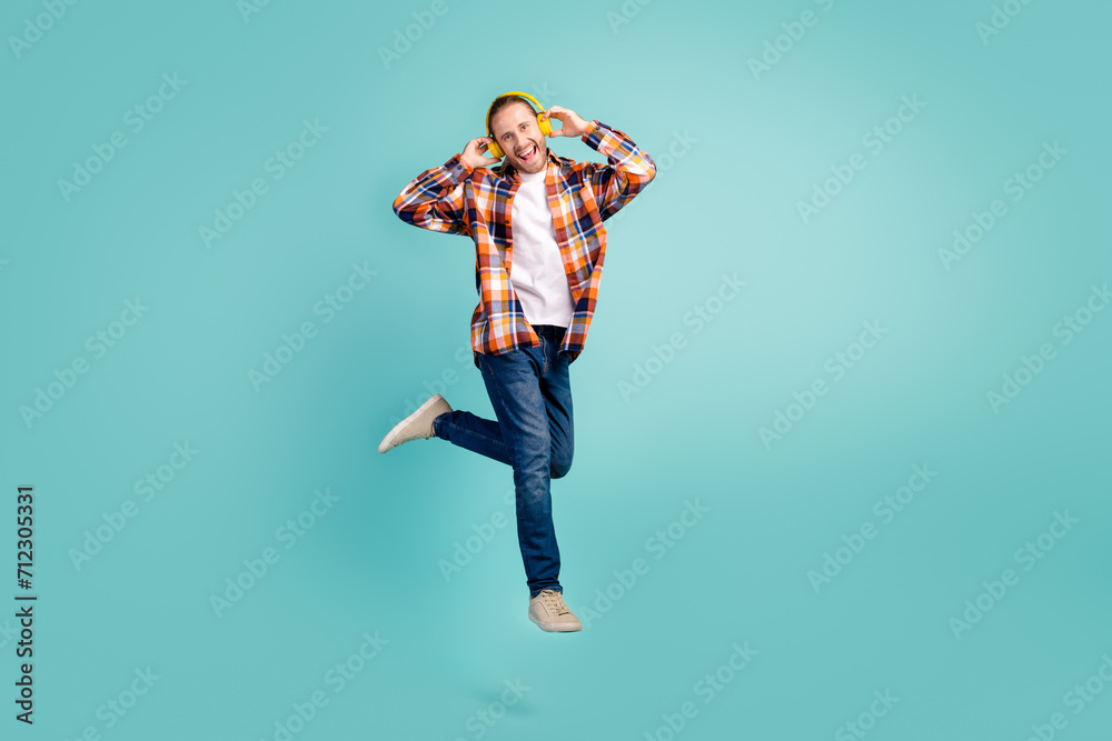 Sticker Full length photo of cool man wear flannel shirt jeans flying listen rock music in headphones isolated on turquoise color background