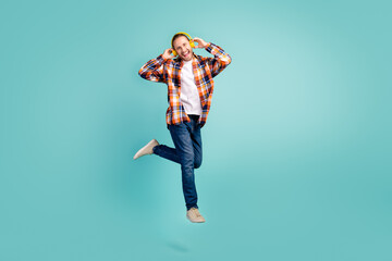 Full length photo of cool man wear flannel shirt jeans flying listen rock music in headphones isolated on turquoise color background