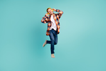 Full length photo of satisfied man wear flannel shirt jeans flying enjoy pop music in headphones...