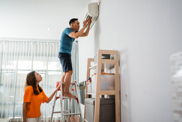 asian man repairs broken air conditioner with his partner