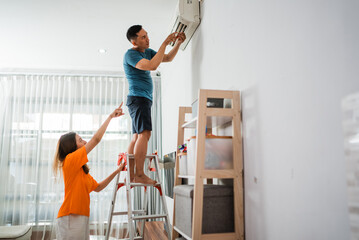 asian man fixs broken air conditioner with his partner pointing gesture