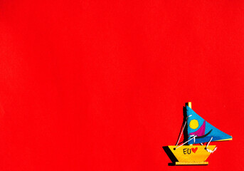 Barco a vela de madeira e velas de tecido de cor azul no fundo vermelho. 