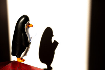 Pinguim de geladeira de cores preta, branca e amarela com sombra projetada na parede.