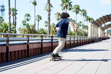 Hipster boy sliding on skateboard along sunny street.