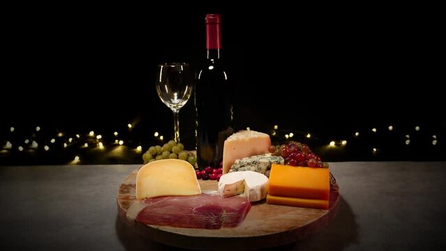 Cheese platter and red wine. Pouring red wine into glass standing on a cheese board with different kinds of cheese. Nicely served selection of exquisite cheese on a black background and wine tasting