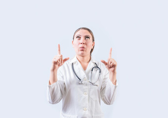 Amazed female doctor pointing a promotion up. Female doctor looking and pointing up isolated