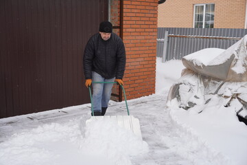 A man cleans snow in the winter in the courtyard of the house.