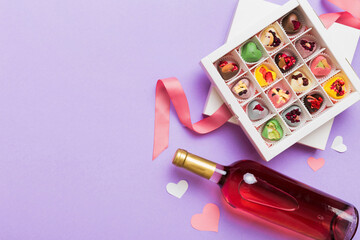 Bottle of red wine on colored background for Valentine Day with gift and chocolate. Heart shaped with gift box of chocolates top view with copy space
